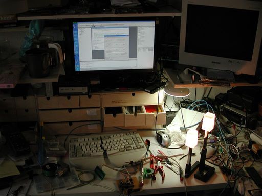 Desk cluttered with electronics, keyboard and monitor in background